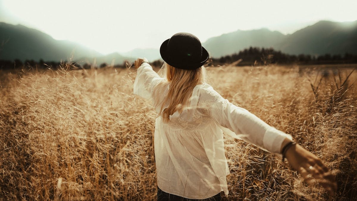 A woman in a field, arms outstretched, enjoying a peaceful autumn day.